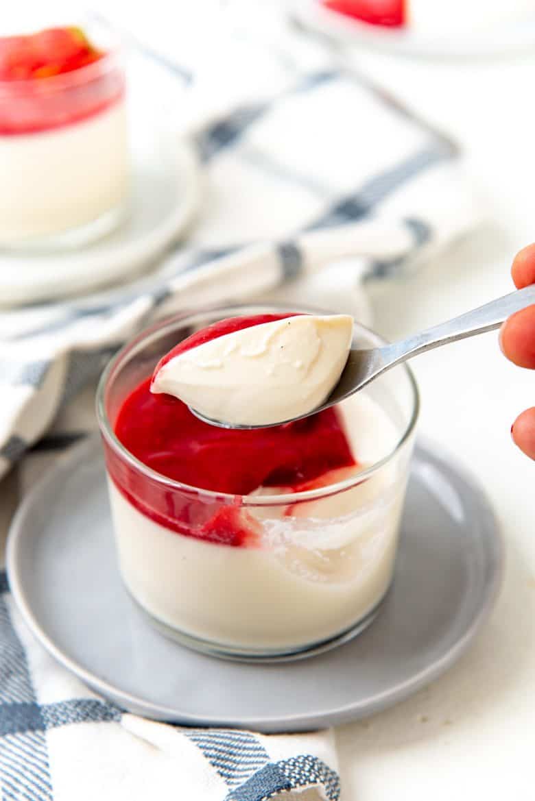 A spoonfu of silky smooth panna cotta held over the single serving of panna cotta