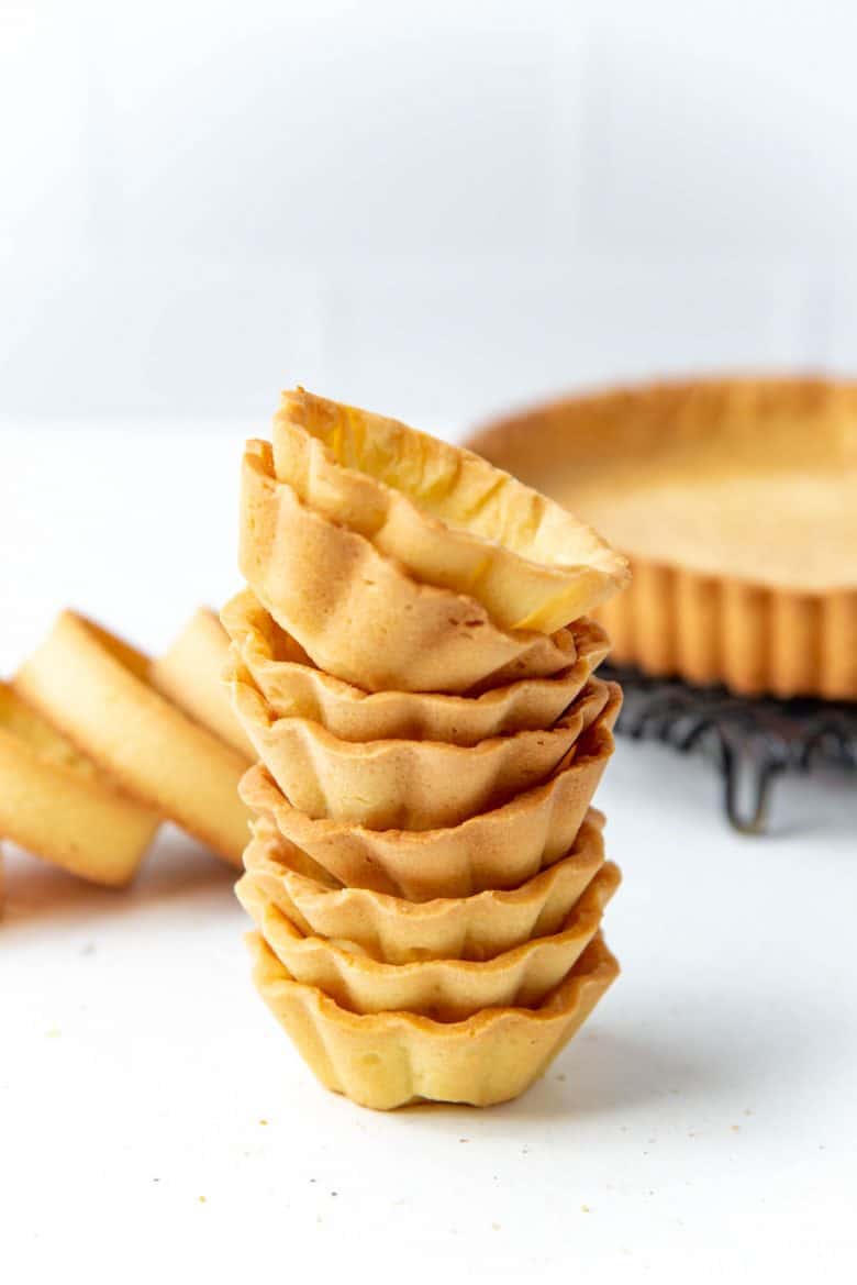 Mini fluted tart shells stacked on top of each other with more pate sucree shells in the background