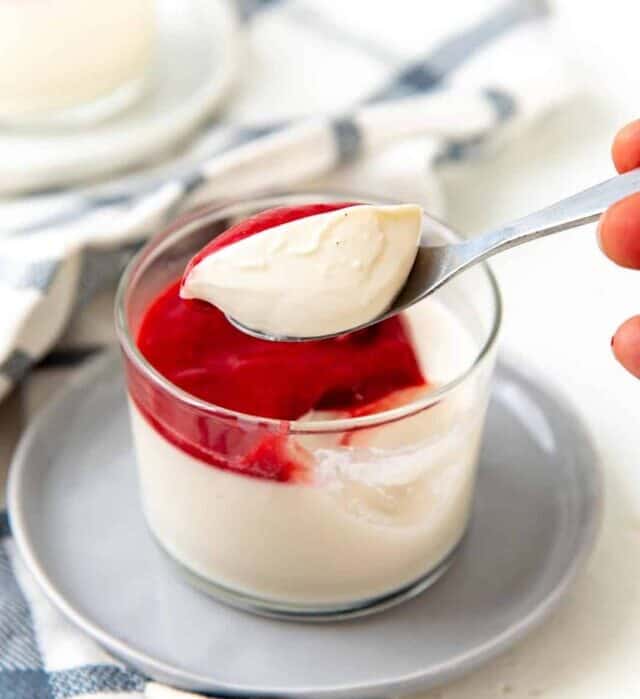 A spoonfu of silky smooth panna cotta held over the single serving of panna cotta