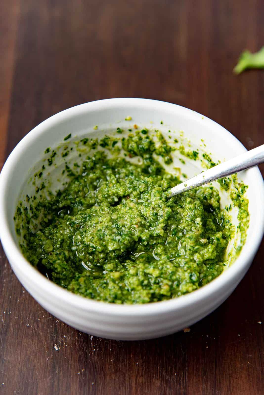 Parsley pesto in a small white bowl after adding olive oil and mixed with a spoon.
