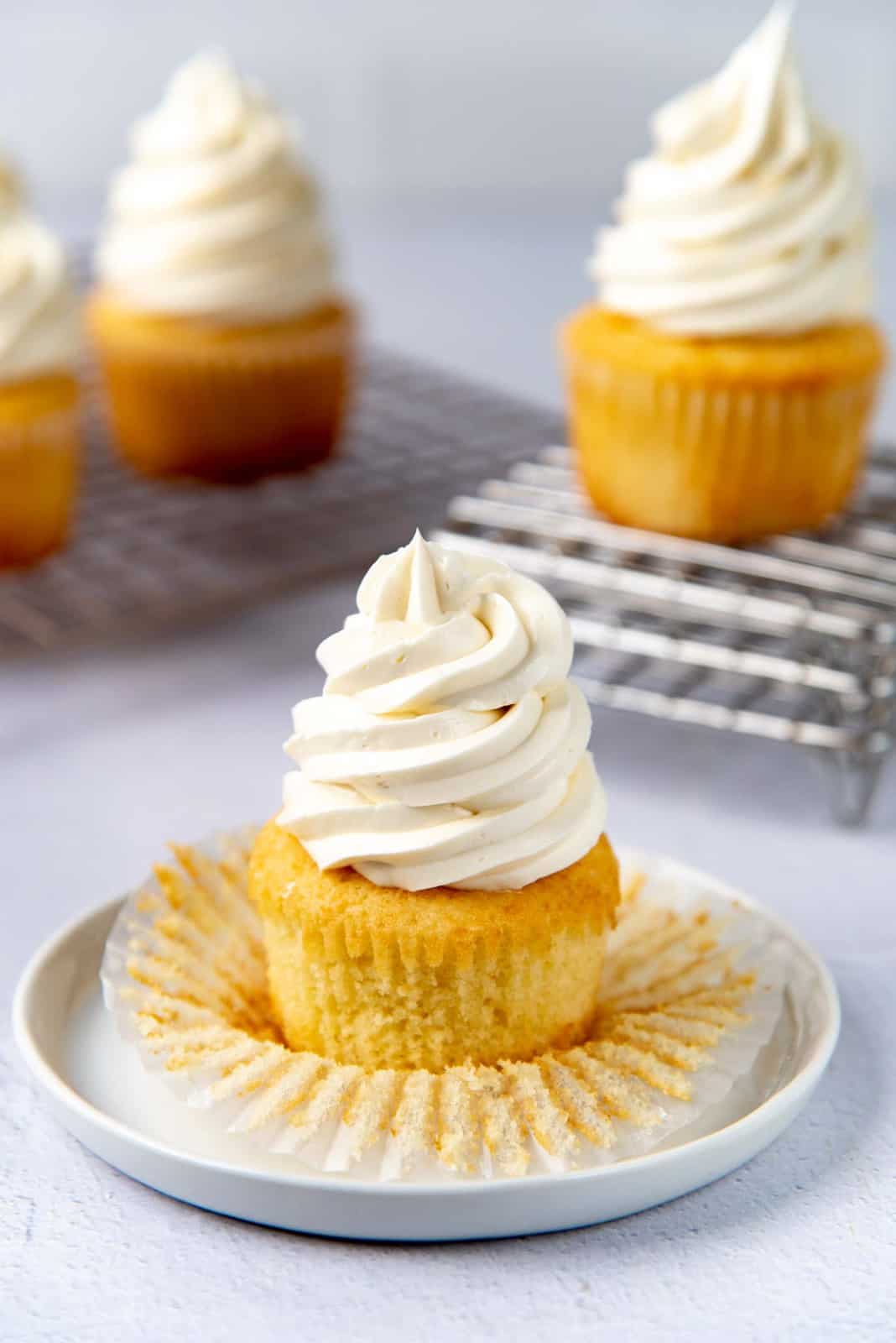 Unwrapped vanilla cupcakes piped with vanilla frosting on a white plate