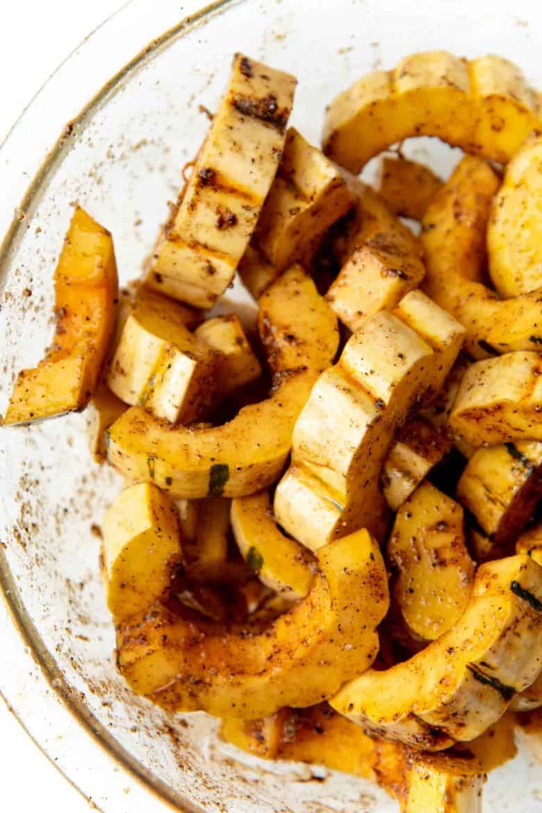 Delicata squash sliced and tossed with oil and seasoning in a bowl