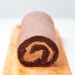 Chocolate Swiss roll cake dusted with powdered sugar on top on a serving platter.