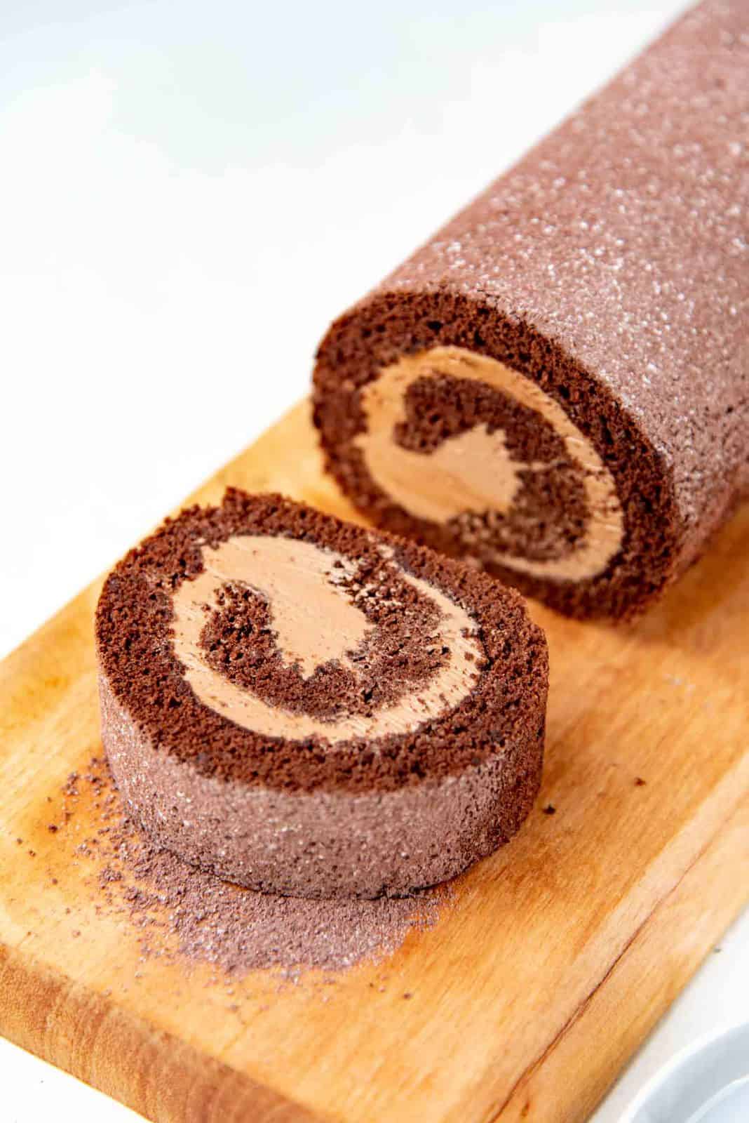 Chocolate swiss roll on a brown serving platter, with a slice cut