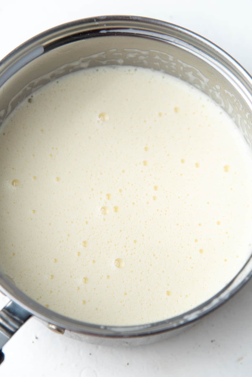 Heated eggnog custard base in a saucepan.
