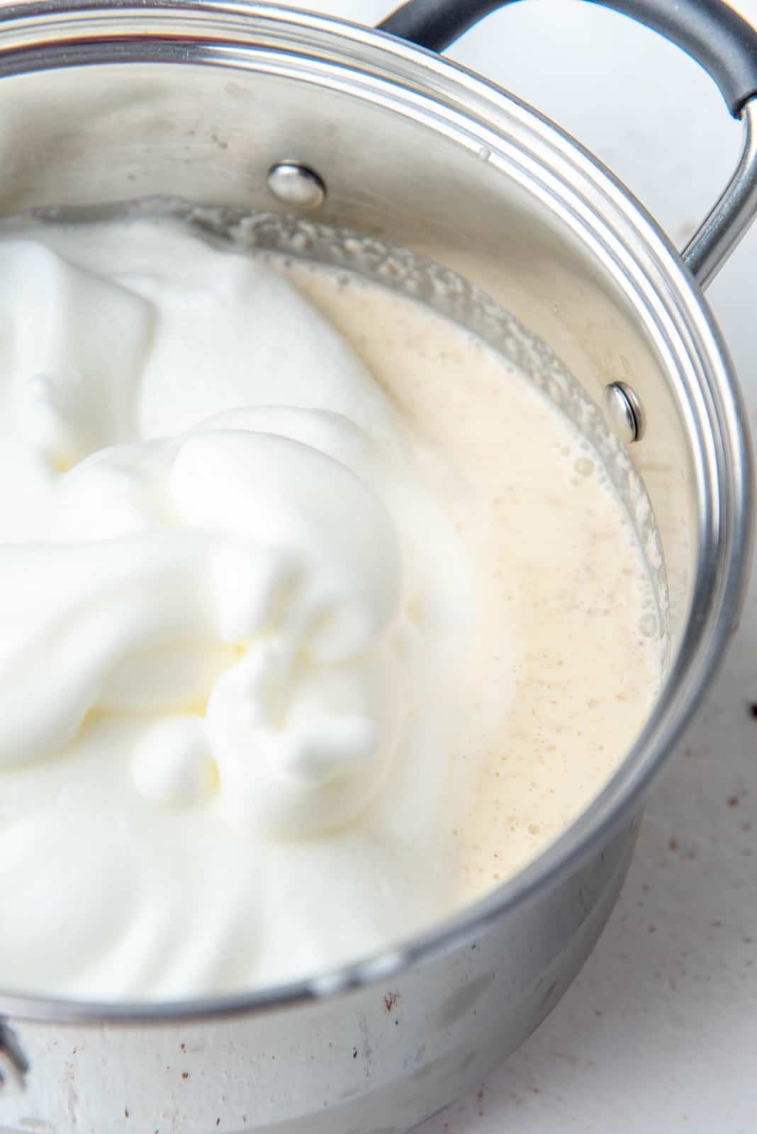 Egg white form being mixed into the eggnog mixture in the saucepan.