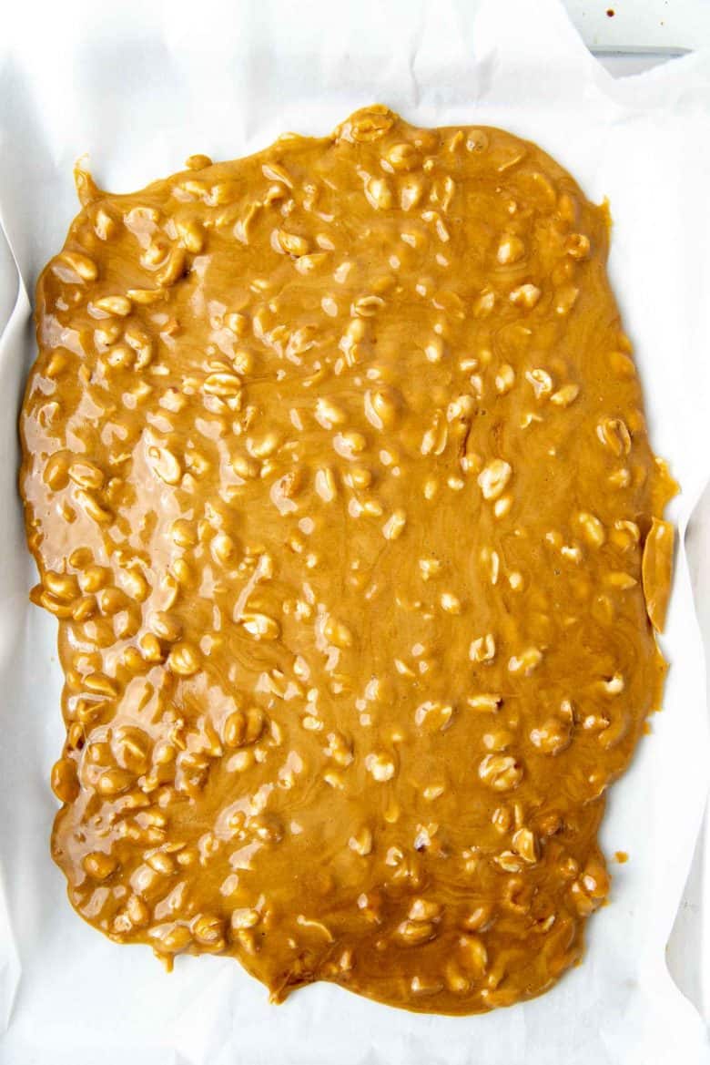 Peanut brittle mixture spread on a parchment paper lined baking tray