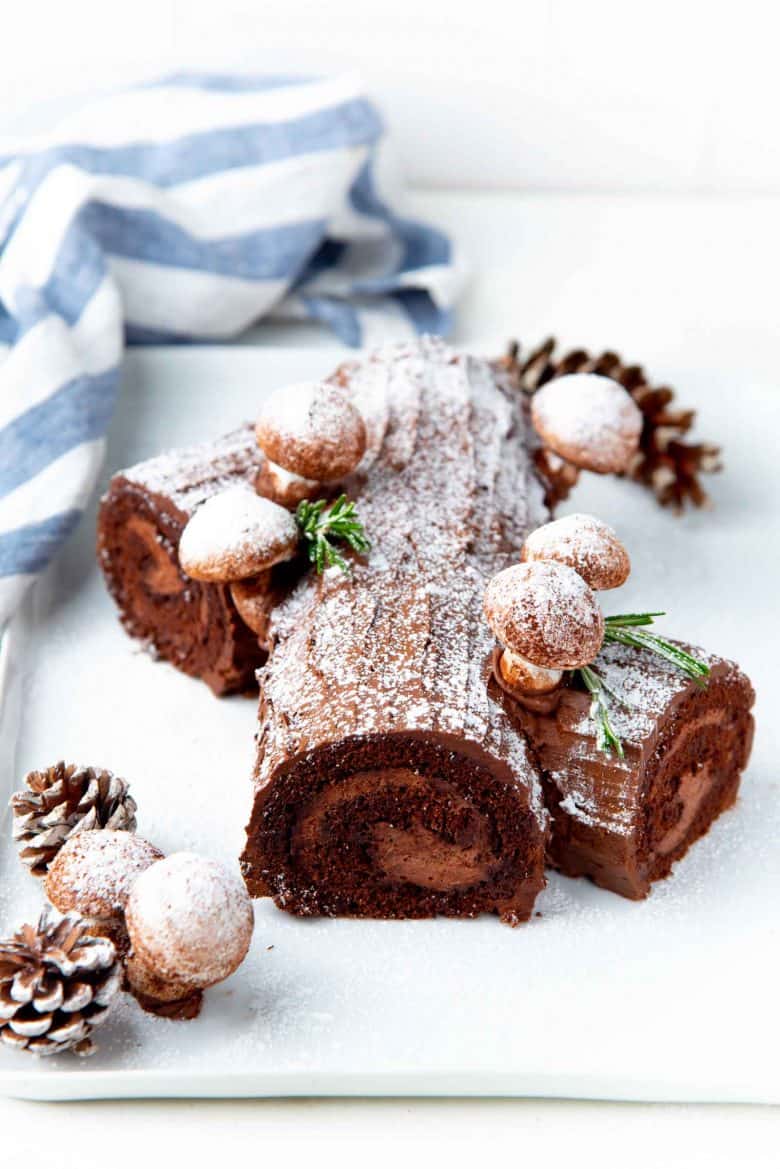 An angled view of a branched buche de noel with meringue mushroom decorations and coated in whipped ganache