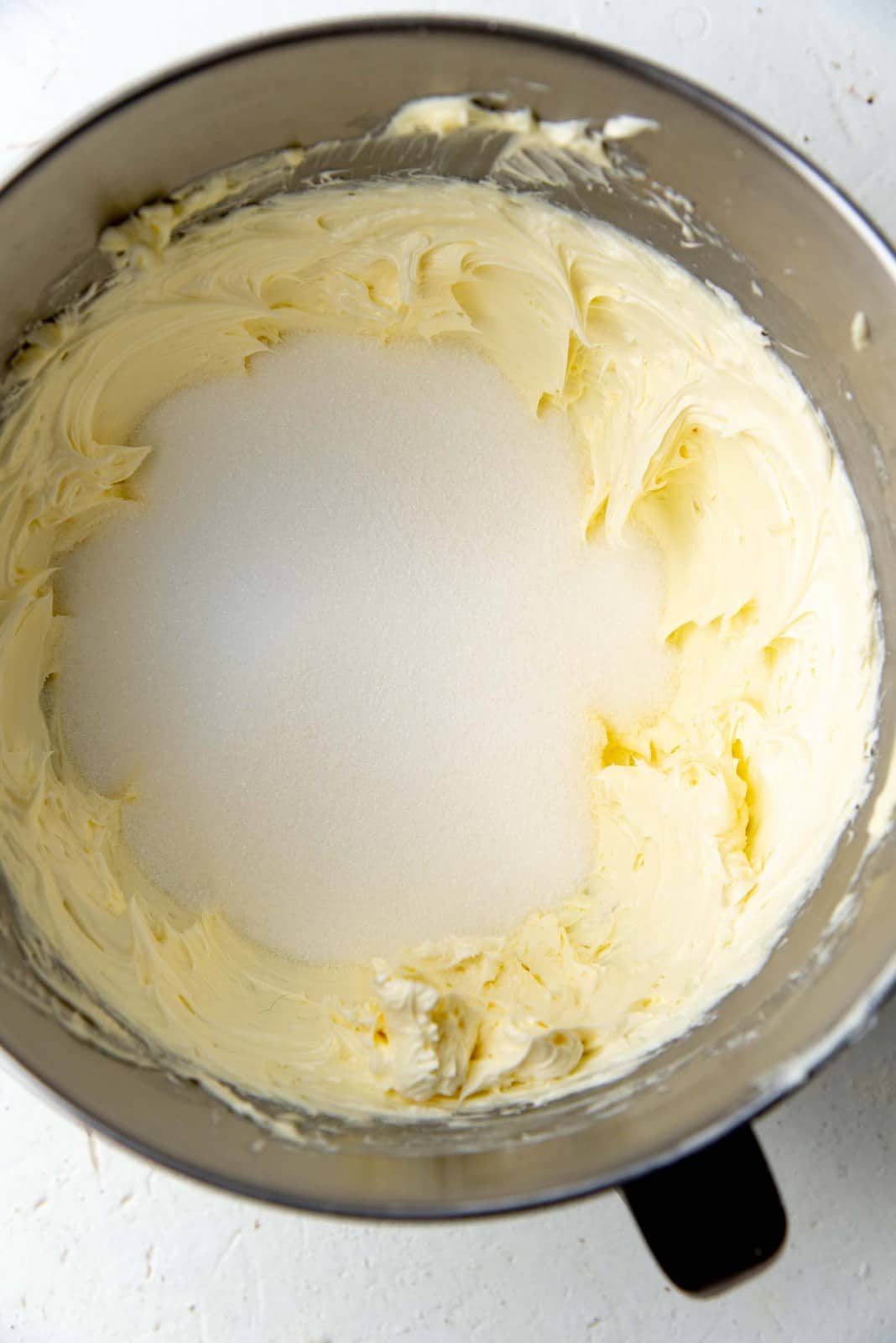 Adding sugar to creamed butter in a mixing bowl