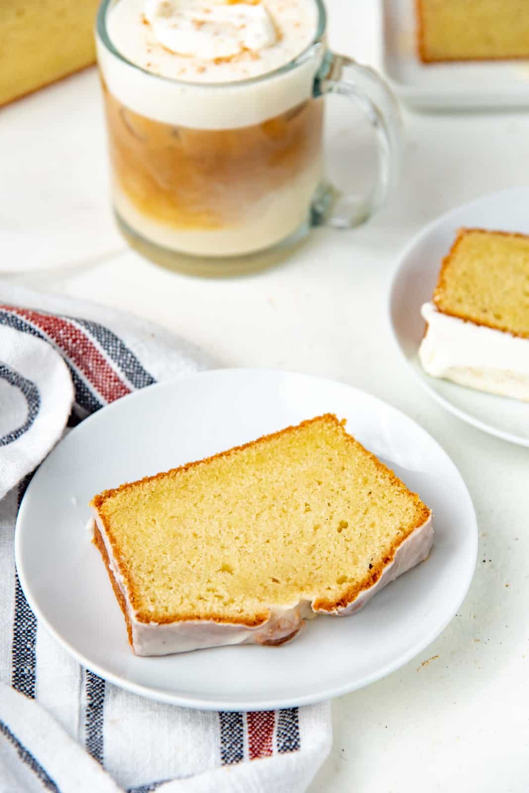 Glazed eggnog cake slice on a plate, with eggnog latte in the background