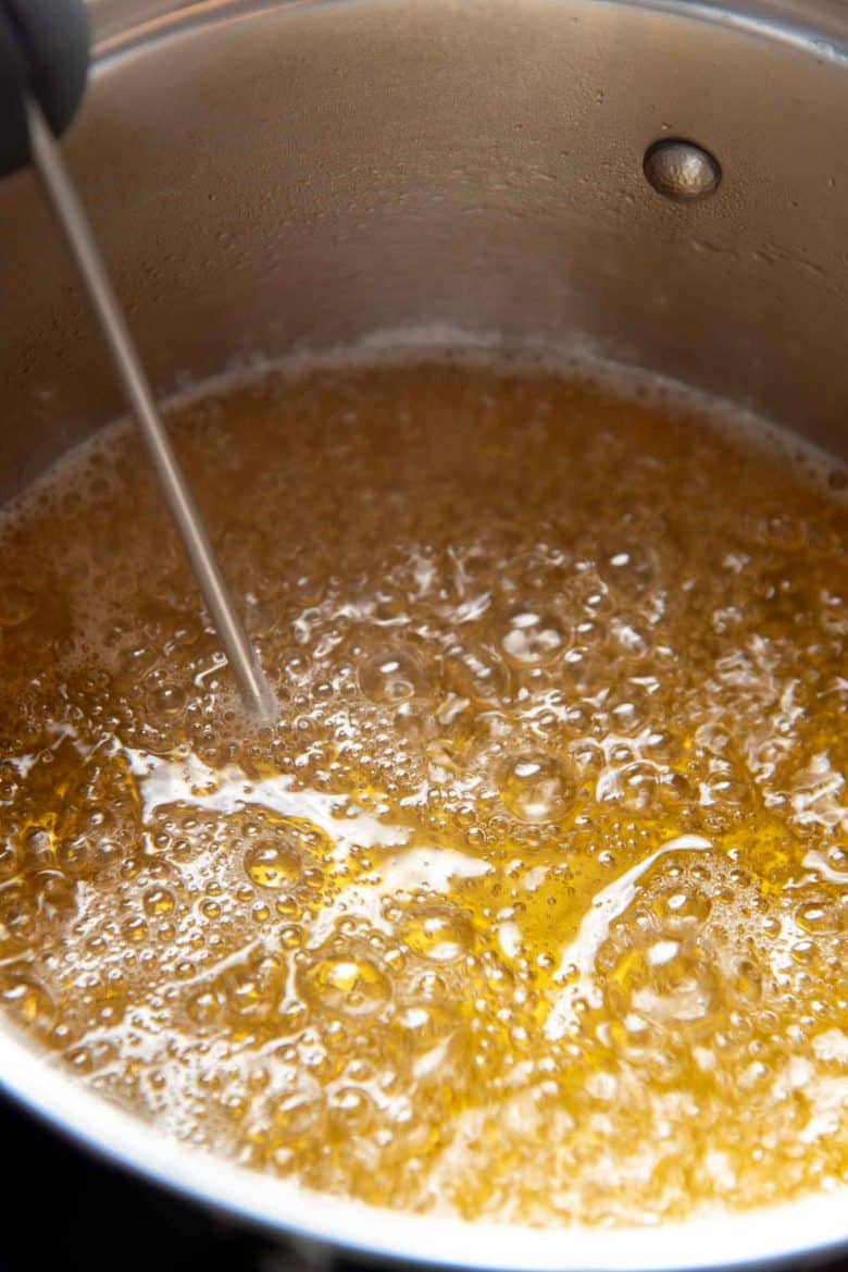 The sugar syrup boiling with a candy thermometer in the pot
