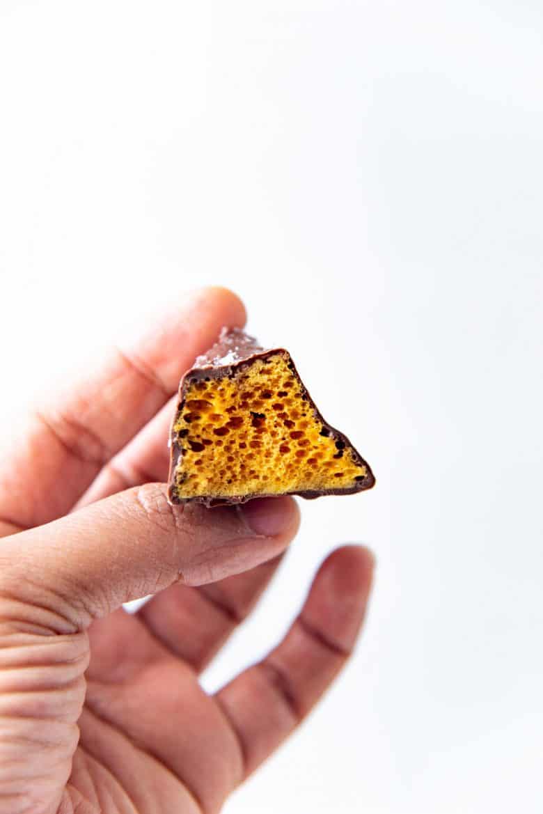 A single chocolate covered honeycomb toffee held up by a hand