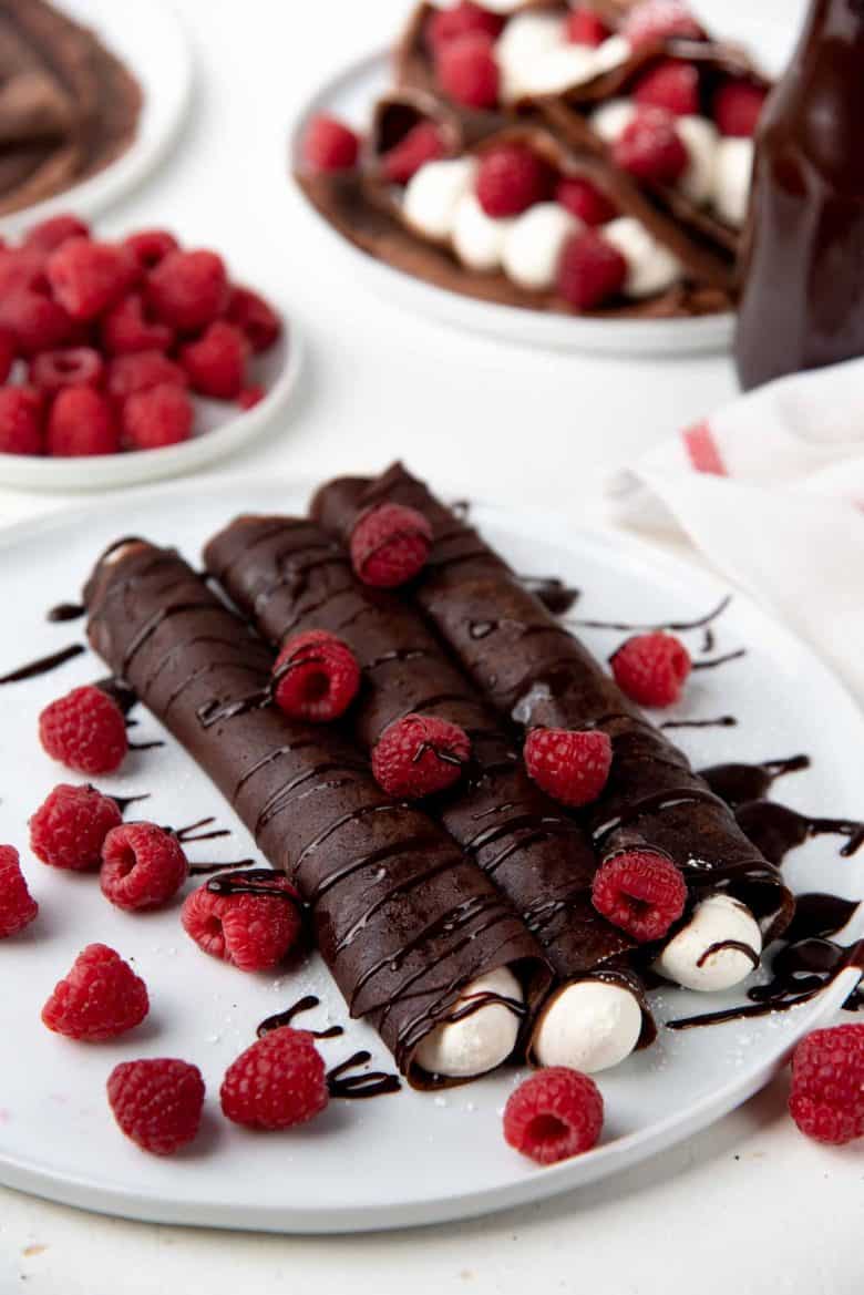 Chocolate crepes rolled up, filled with cream, berries and chocolate sauce