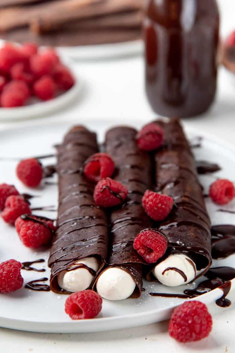 Rolled up crepes with whipped cream, berries and chocolate sauce