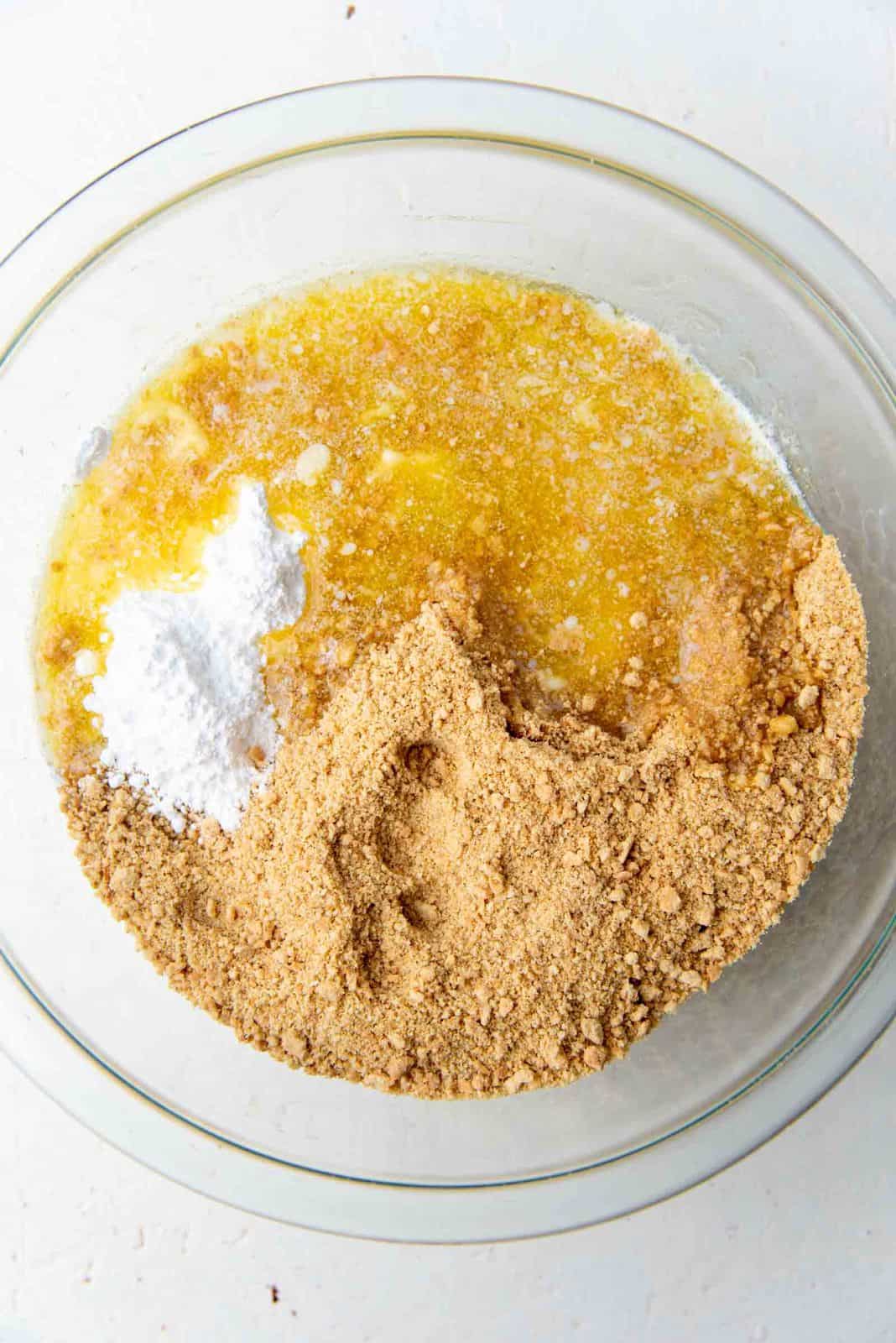 Melted butter added to the bowl of crushed graham cracker crumbs to make the no bake cheesecake crust.