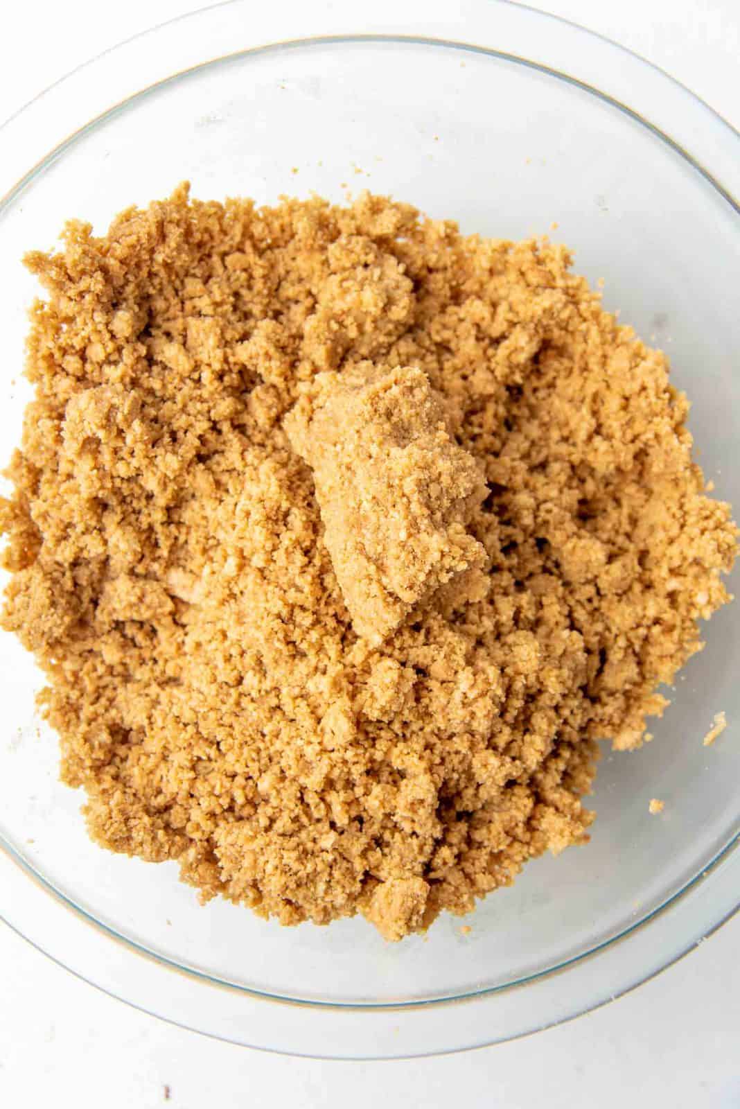 The graham cracker crumb mixture clumped and ready in a glass bowl.