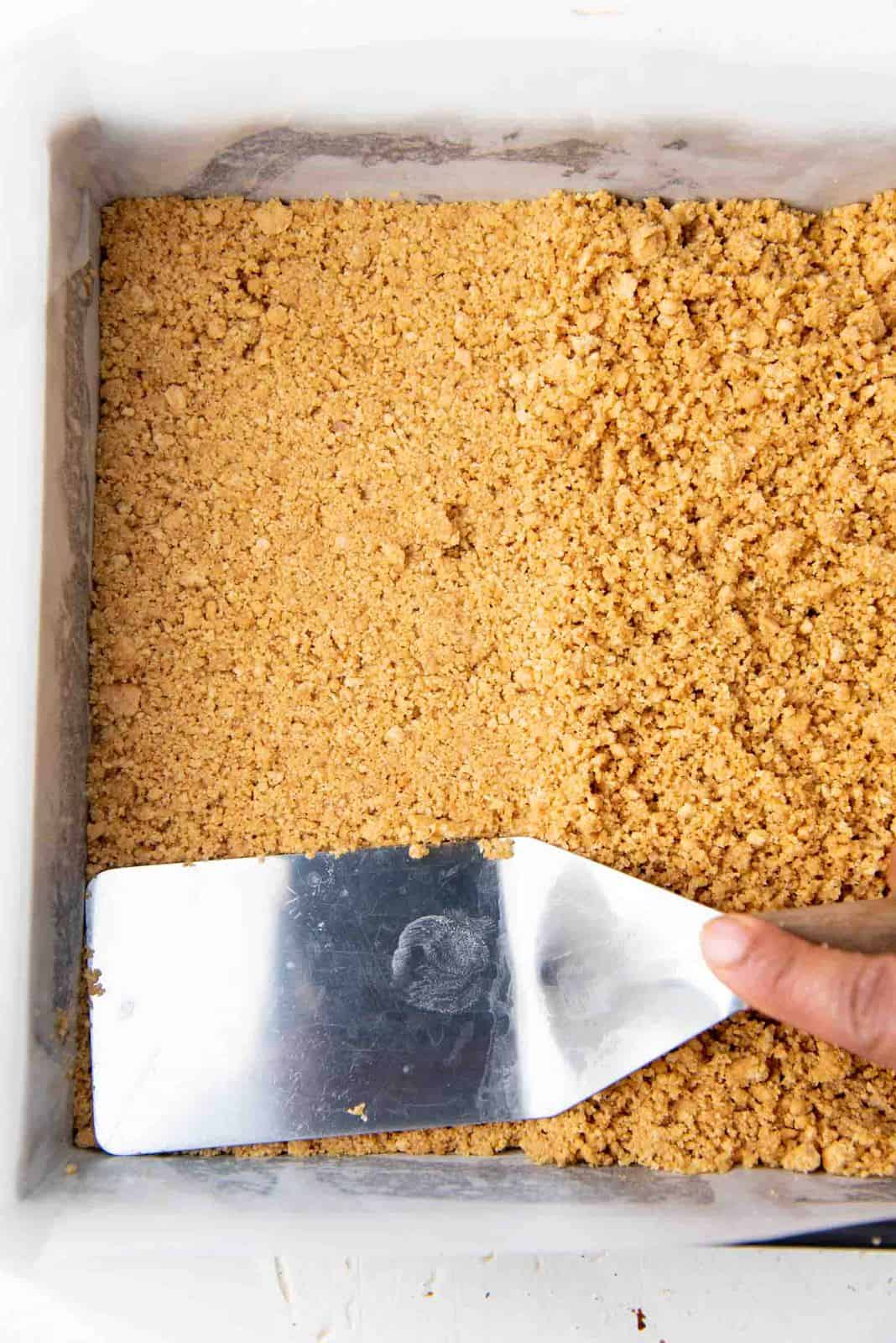 Pressing the graham cracker crumb layer into the bottom of the prepared pan.
