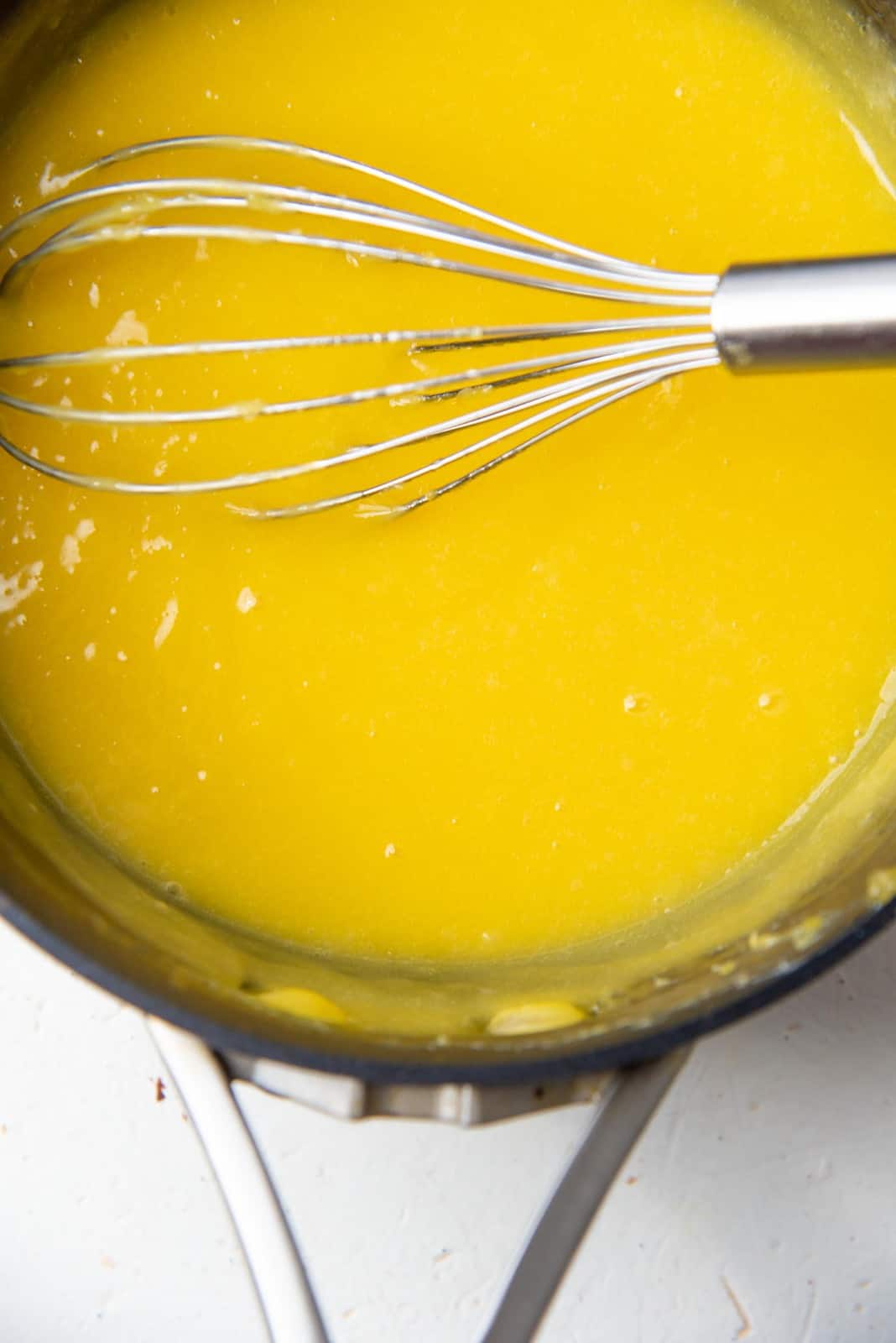 Cooked lemon curd mixture in a saucepan with a wire whisk.