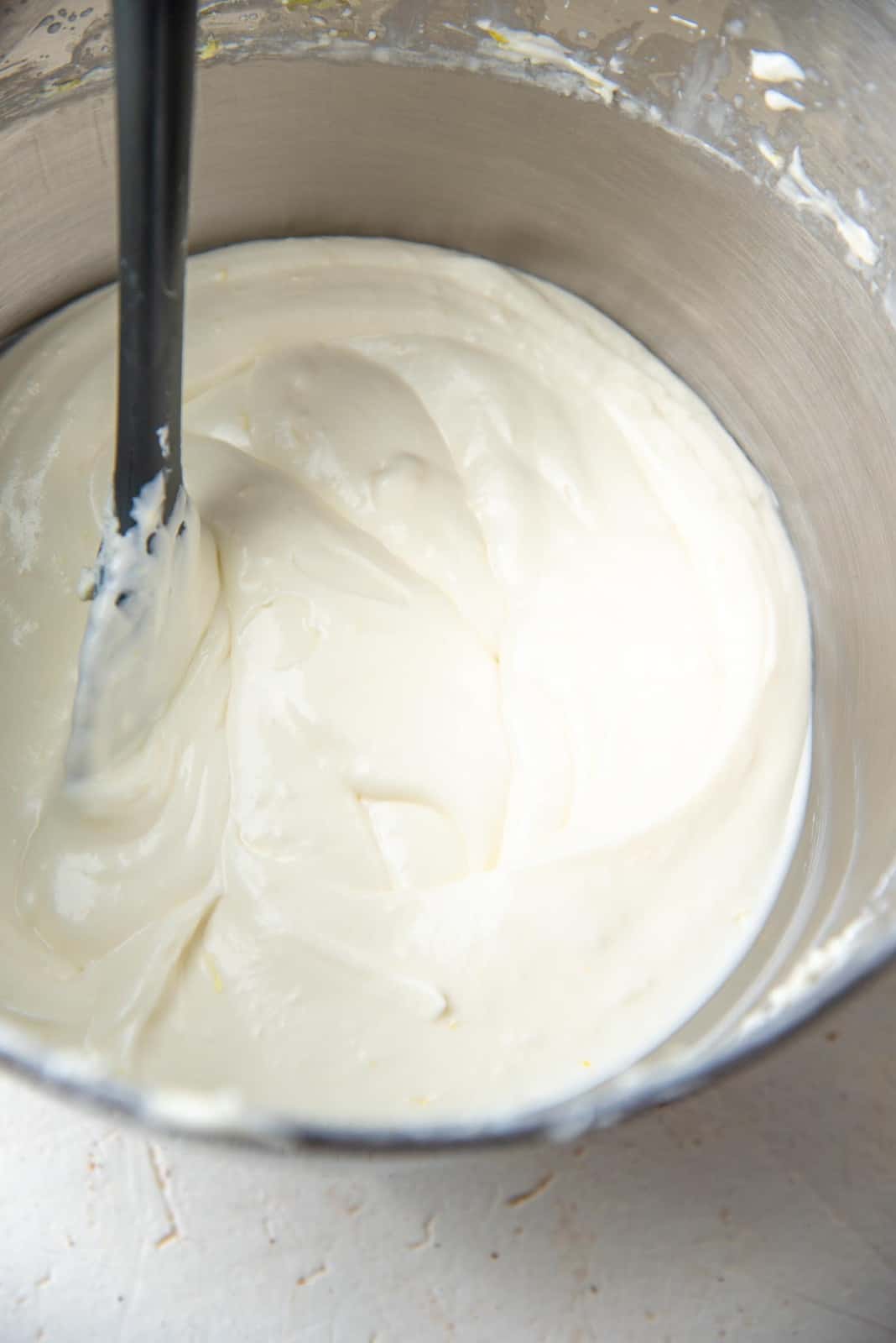 Cream cheese mixture with lemon flavoring in a large metal bowl with a rubber spatula.