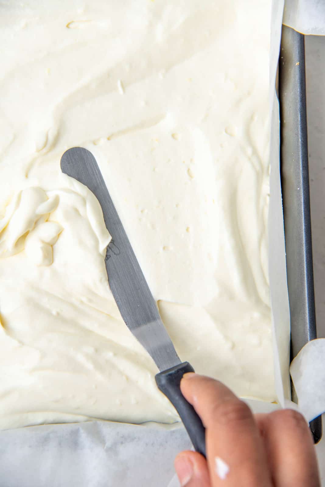 Spreading the lemon cheesecake mixture in the prepared pan over the graham cracker crust.
