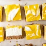 No bake lemon cheesecake bars with a crumbly graham cracker base are neatly arranged on parchment paper.