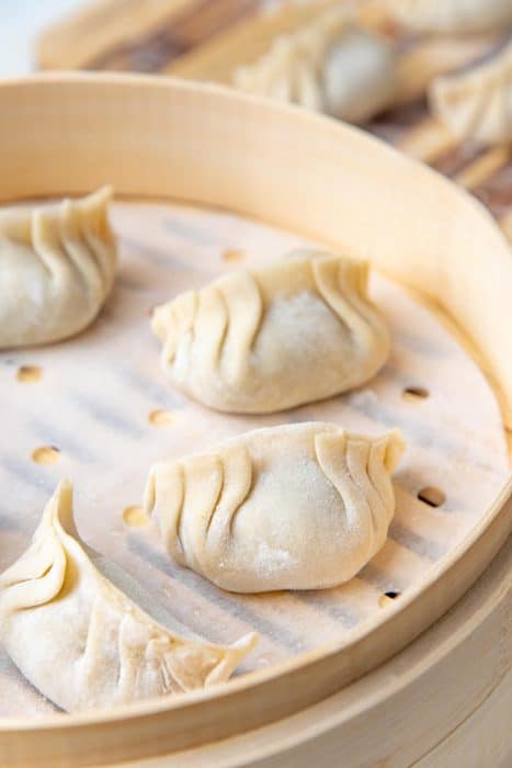 Uncooked, freshly made dumplings placed on parchment paper in a bamboo steamer