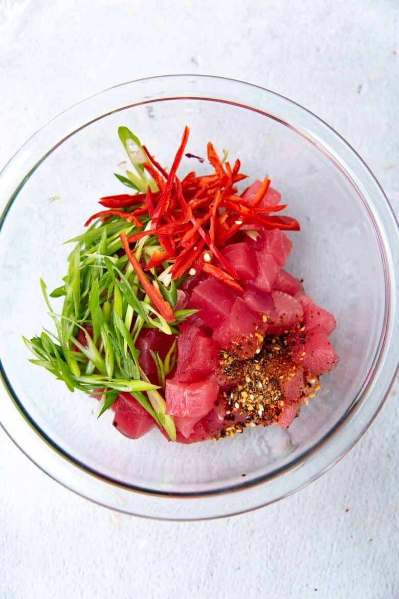Cubed tuna in a bowl with sliced green onions, red chili and shichimi togarashi