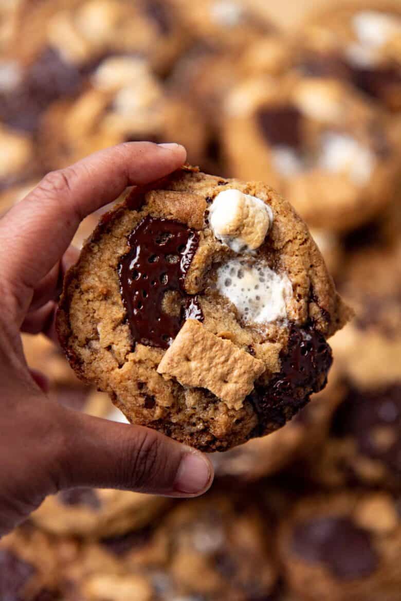 A cookie that is held in a hand, showing the chocolate, melted marshmallows and graham crackers on the surface