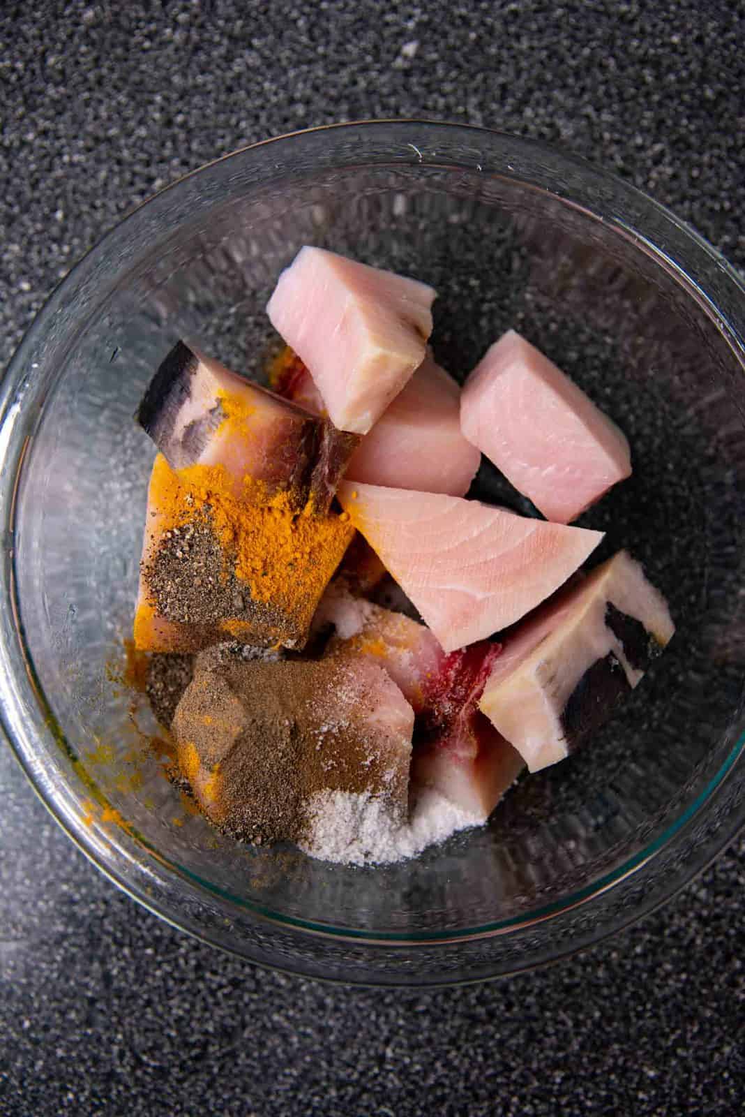 Swordfish cut into pieces in a bowl with the spices