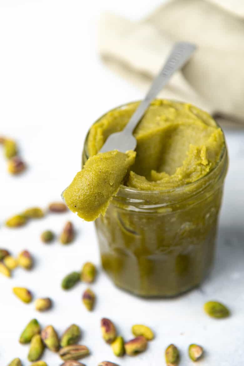 A butter knife with pistachio paste on top of a jar