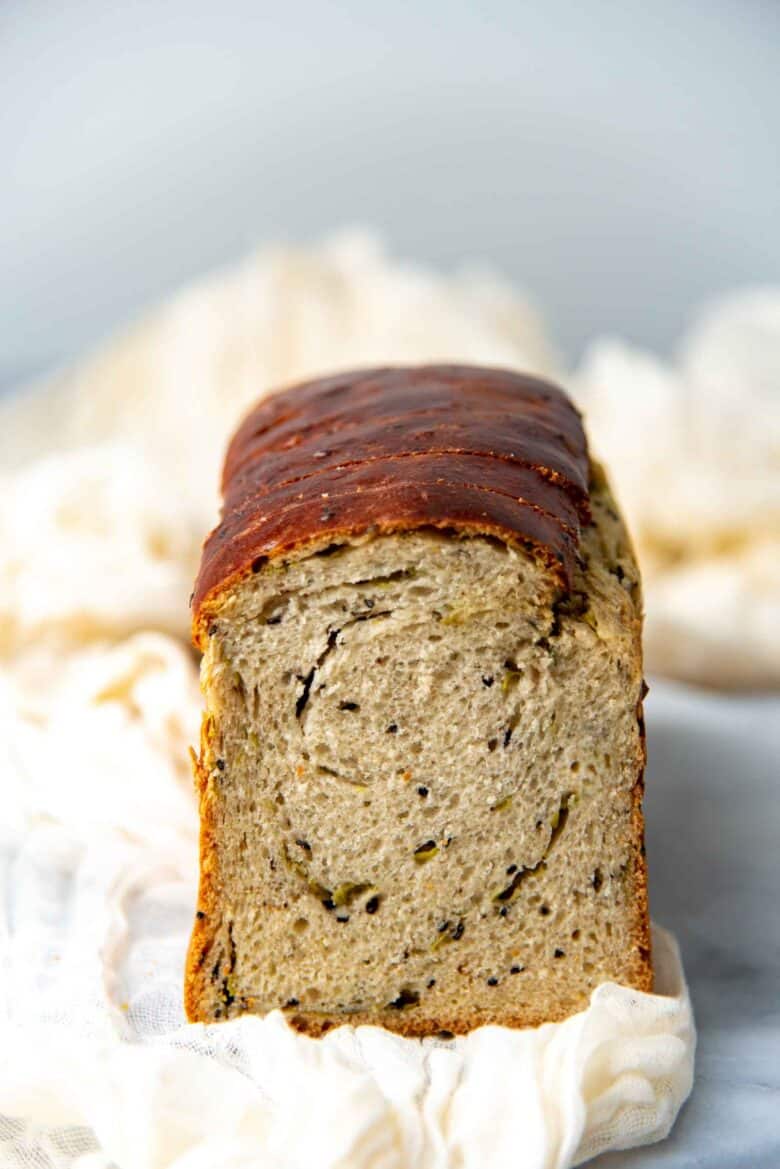 A close up of the cross section of a baked scallion and sesame milk bread loaf, with black sesame seeds and spring onions studded in the dough