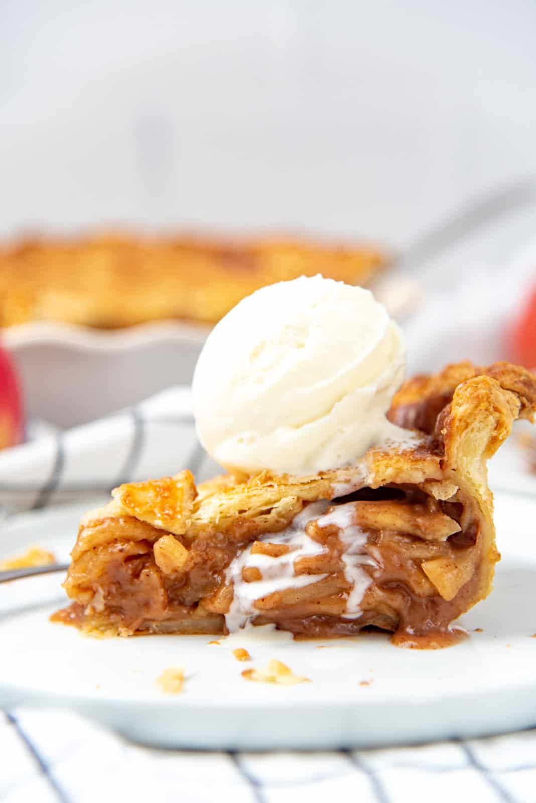 A side on view of a slice of pie with apple filling and a scoop of ice cream on top.