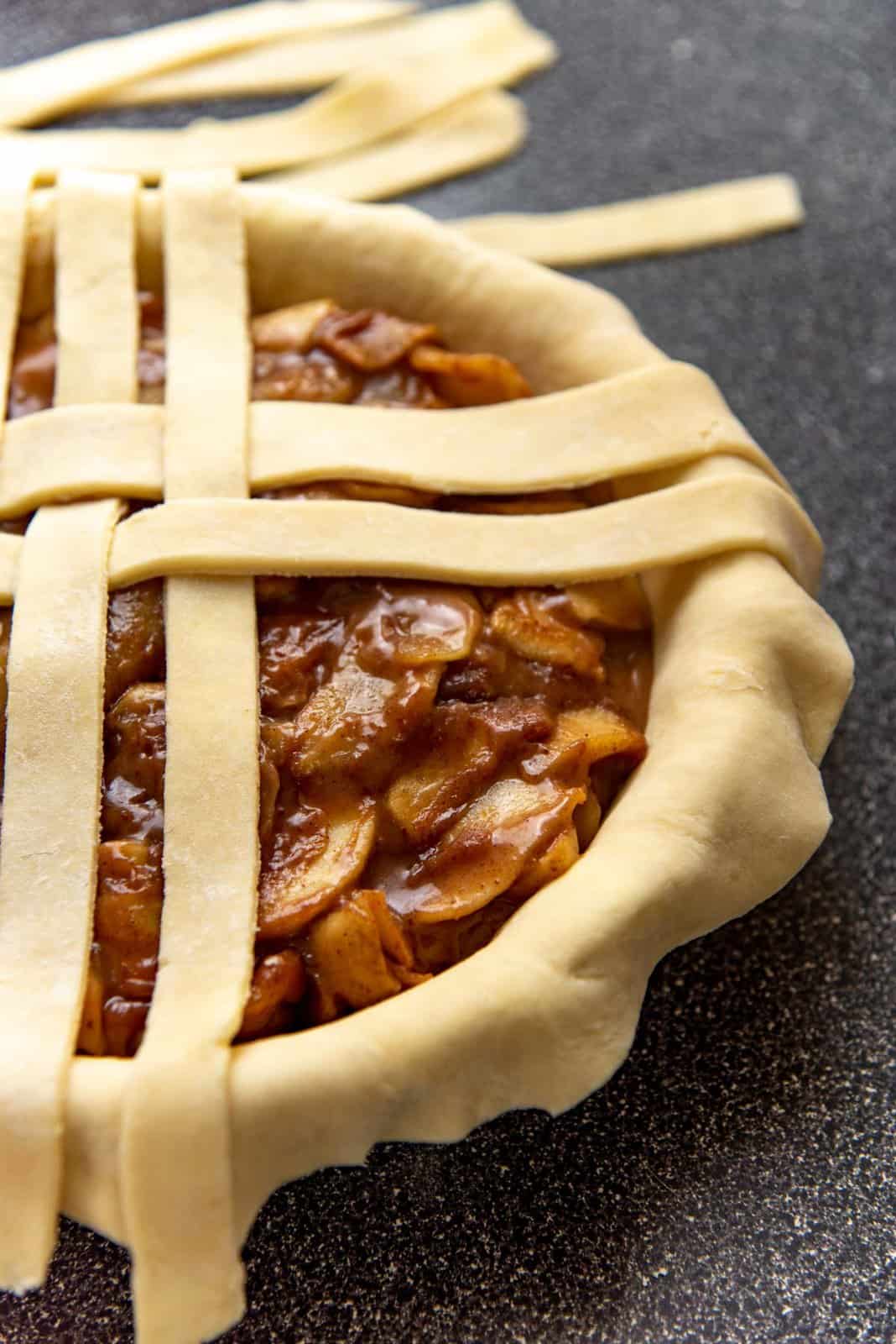 A close up of the apple filling filling the pie plate, with a lattice crust being woven on top.