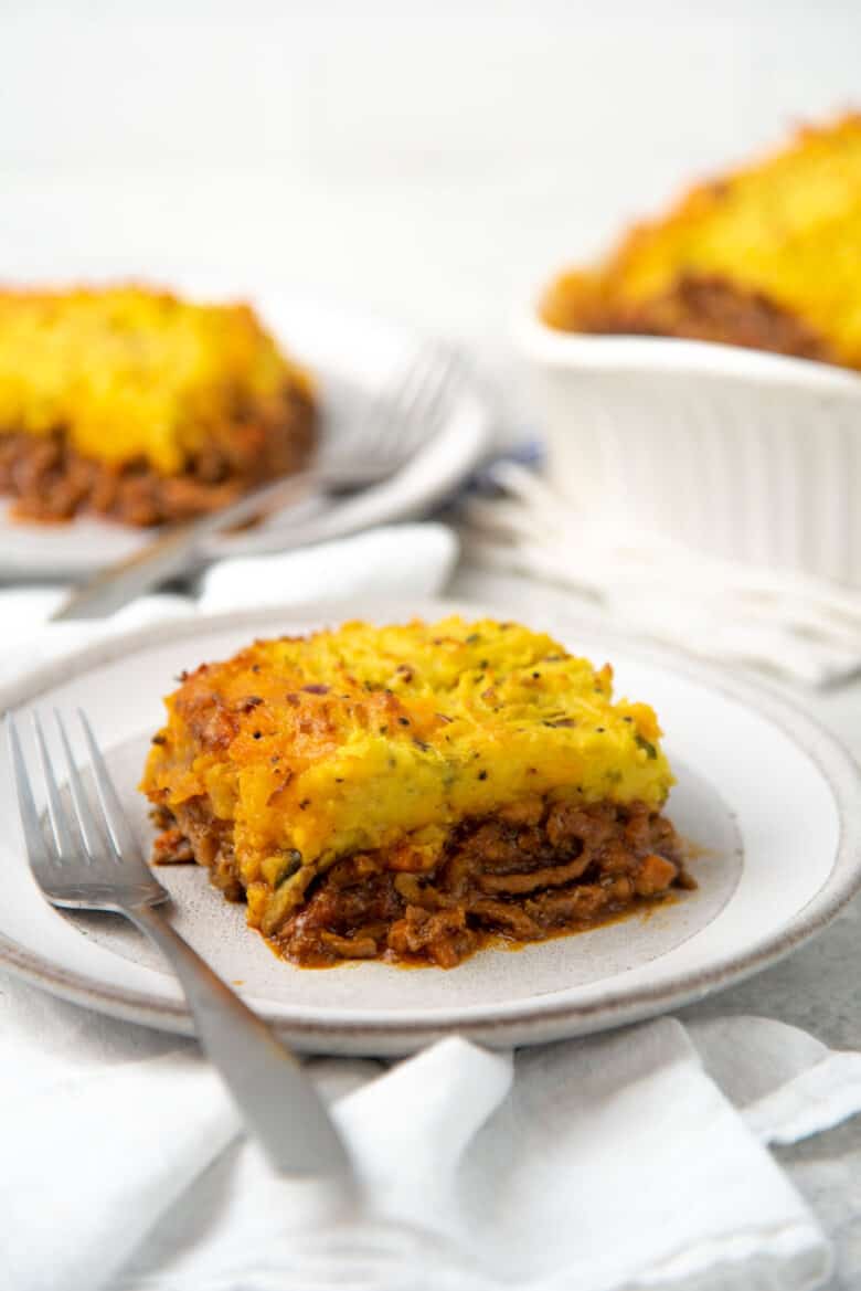 A square slice of curried shepherds pie with a lamb filling and curried potato top, and a fork placed next to it.