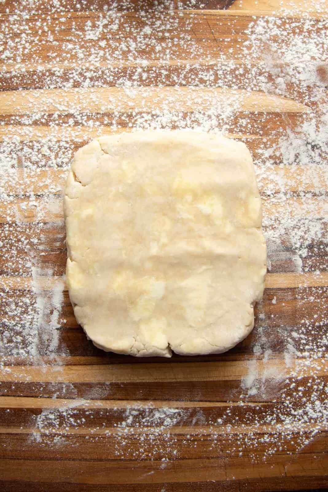 A cold disc of pie dough with pats of butter visible, on a floured surface.