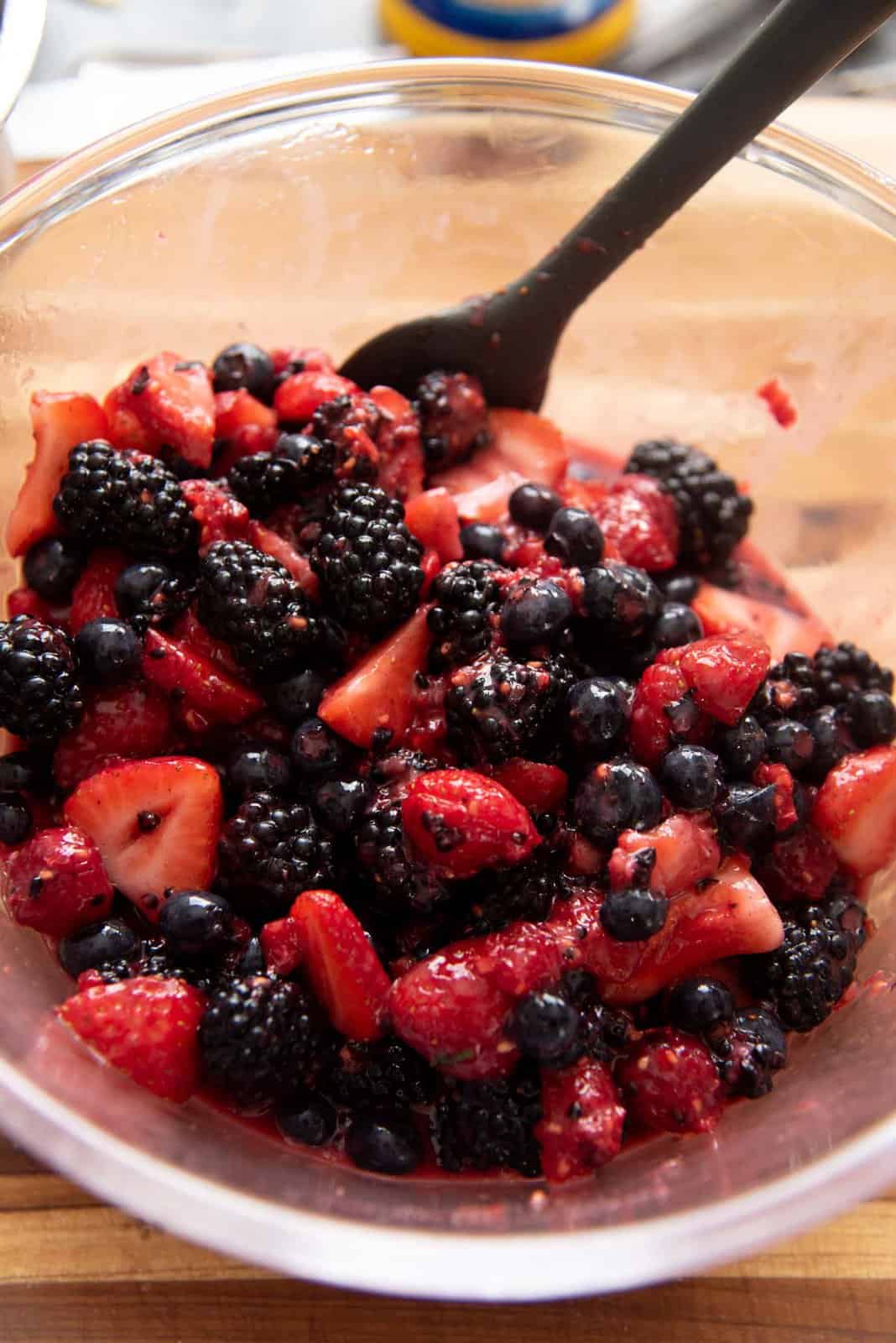 A bowl of berries with whole and crushed berries mixed, with a spatula in the bowl.