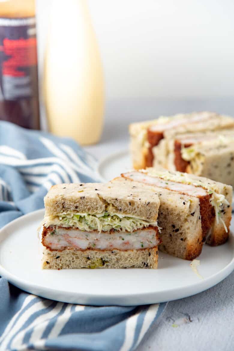 A sandwich made with ebi katsu, cut in half and places on a white plate. 