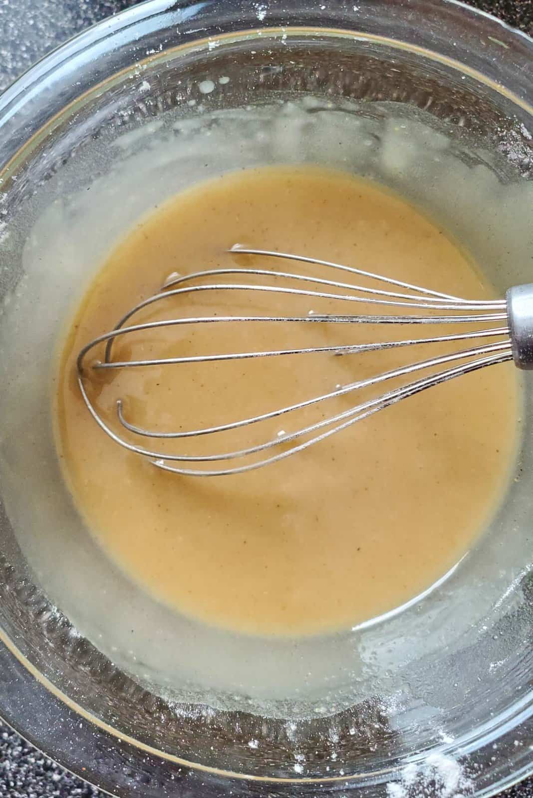 A close up of a light brown paste, that is the oil and flour paste, with a whisk still in the paste.