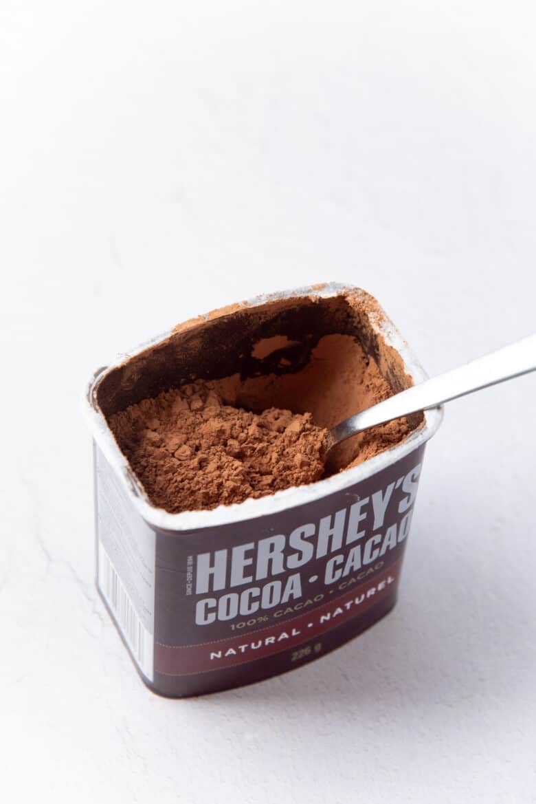 A close up of the inside of a natural cocoa powder container with a spoon inside.