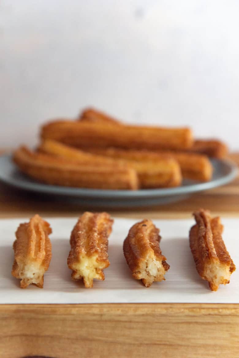 A cross section of the four churros laid out in the foreground, with a plate of churros in the background.
