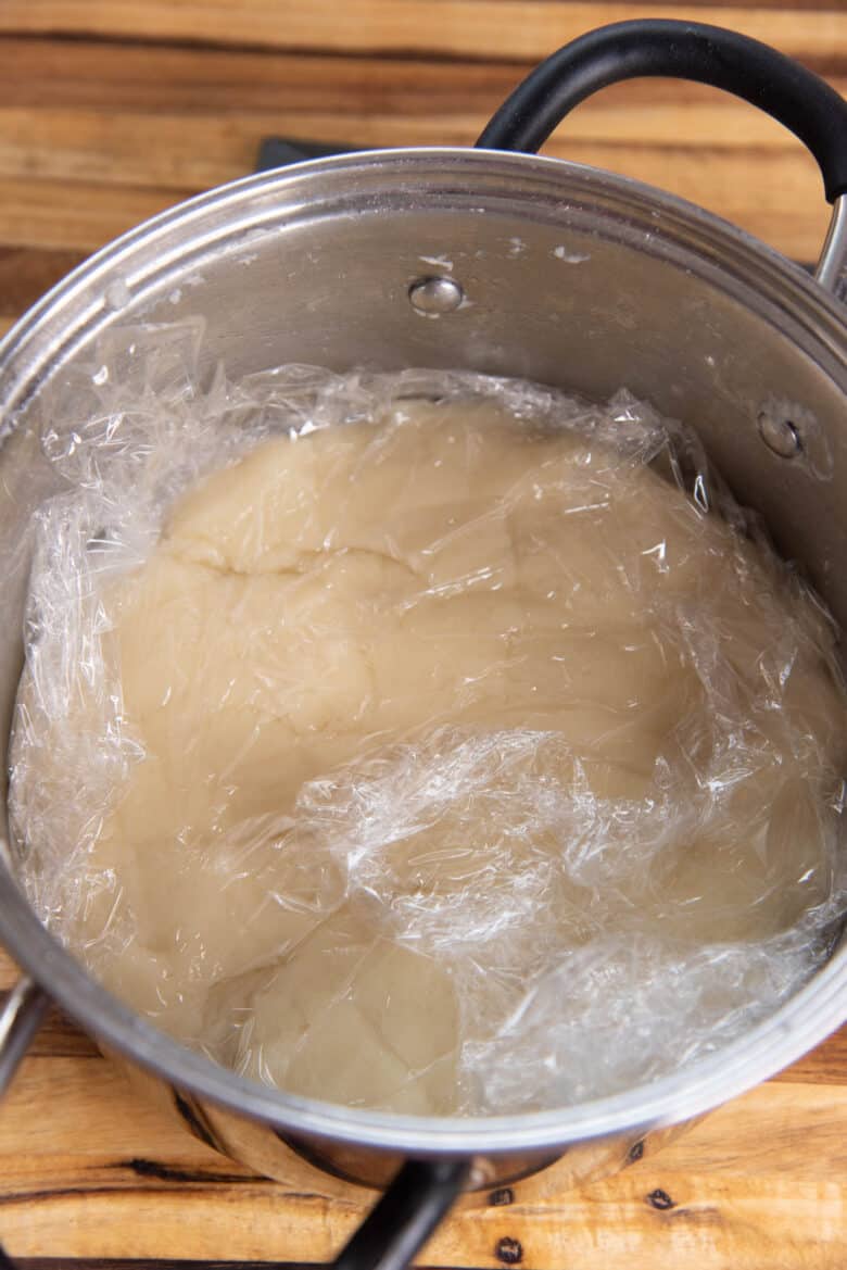 The dough covered with a piece of plastic wrap inside the pot.