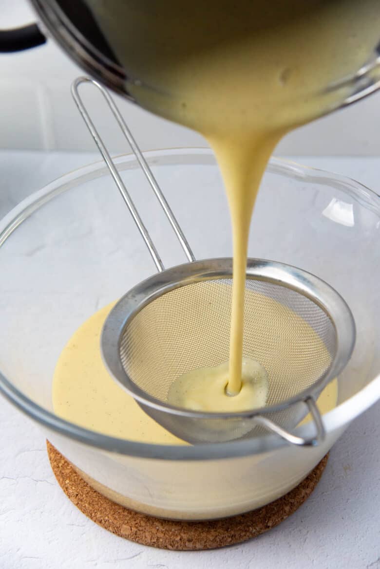 Pouring custard poured into a large glass bowl through a sieve.
