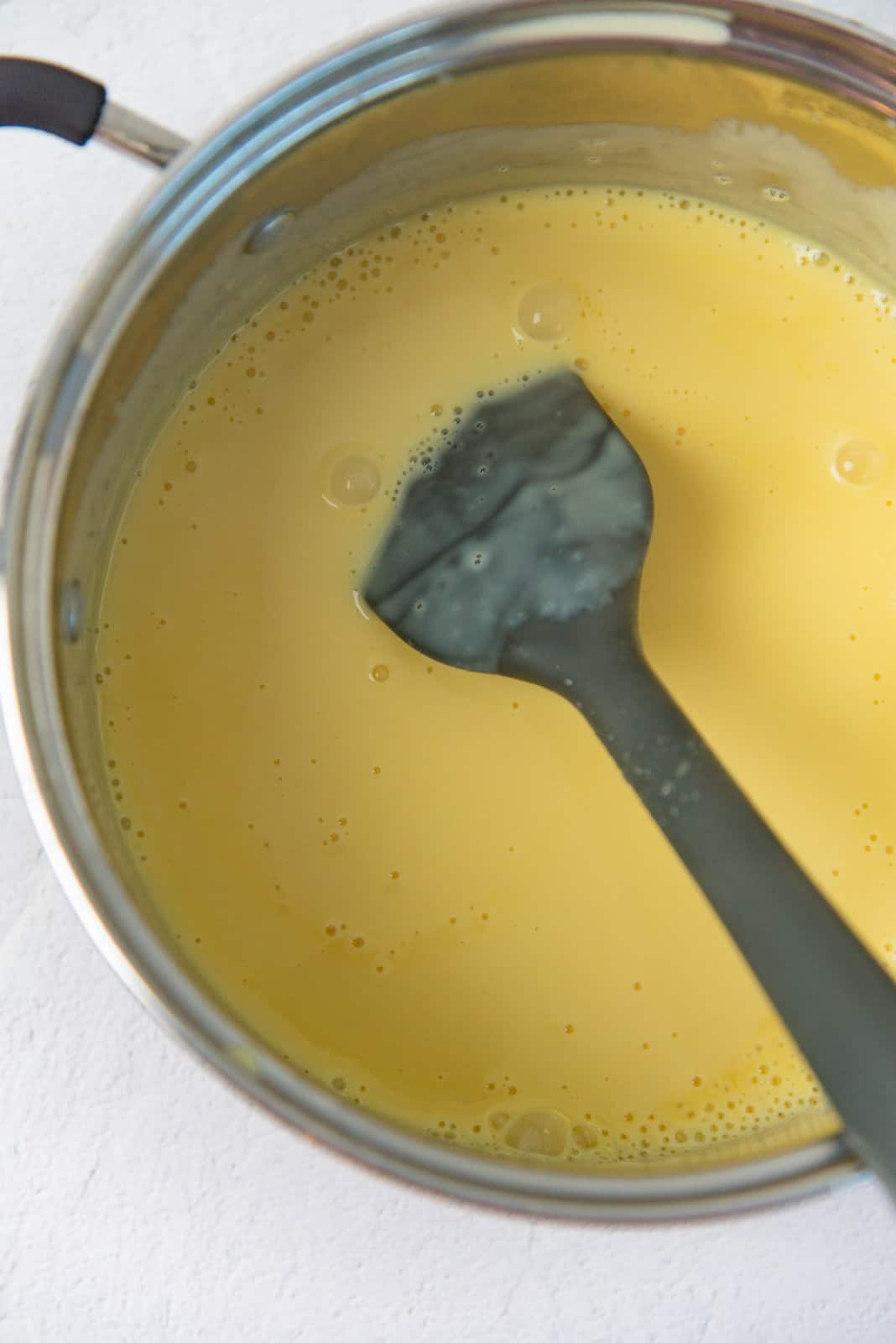 A spatula stirring the custard in a pot.