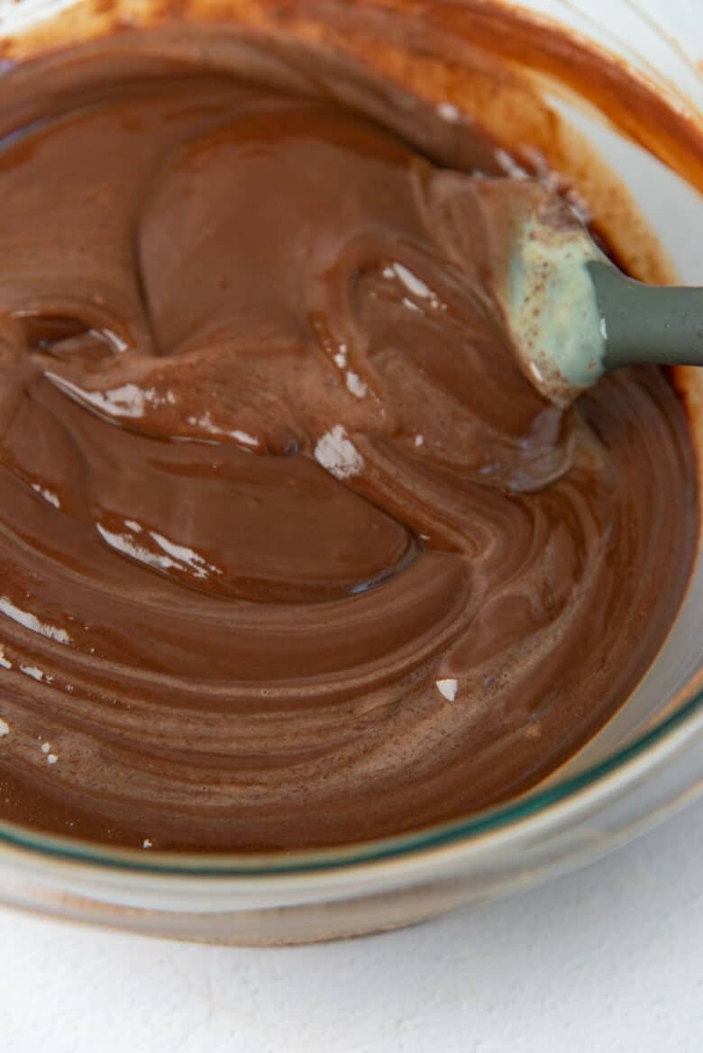 A close up of melted chocolate with streaks of custard, with a spatula stirring the mix.