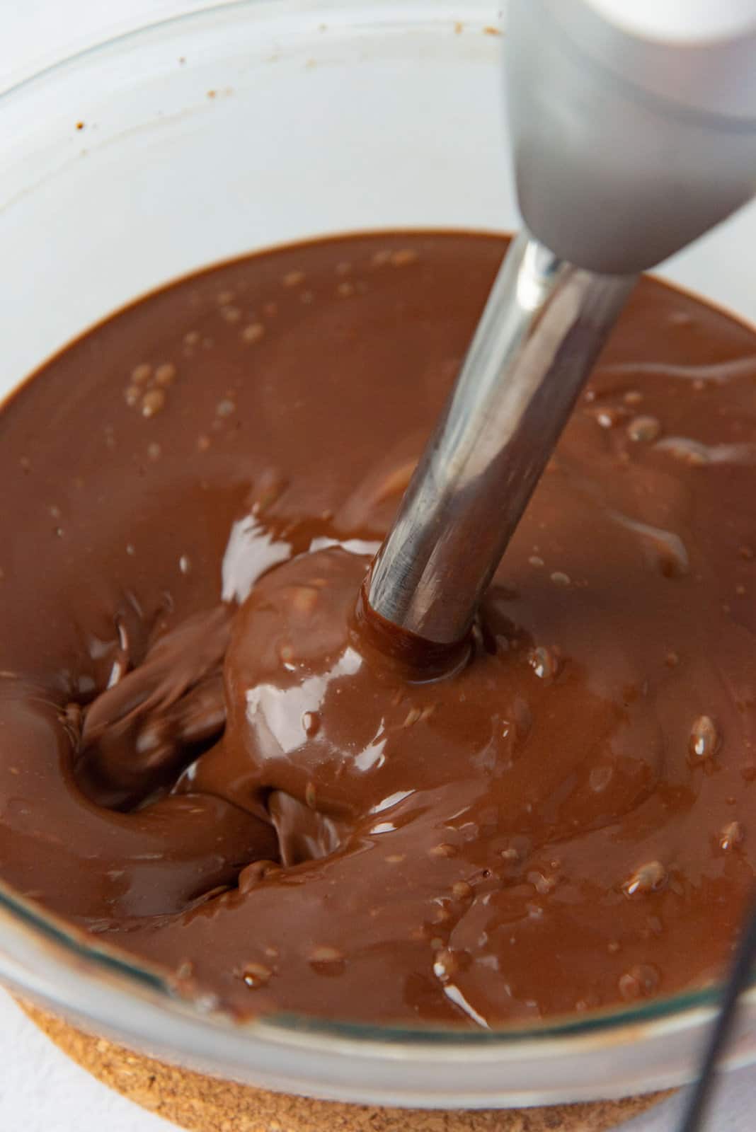 A large bowl of chocolate cremeux, with a stick blender blending the mixture.