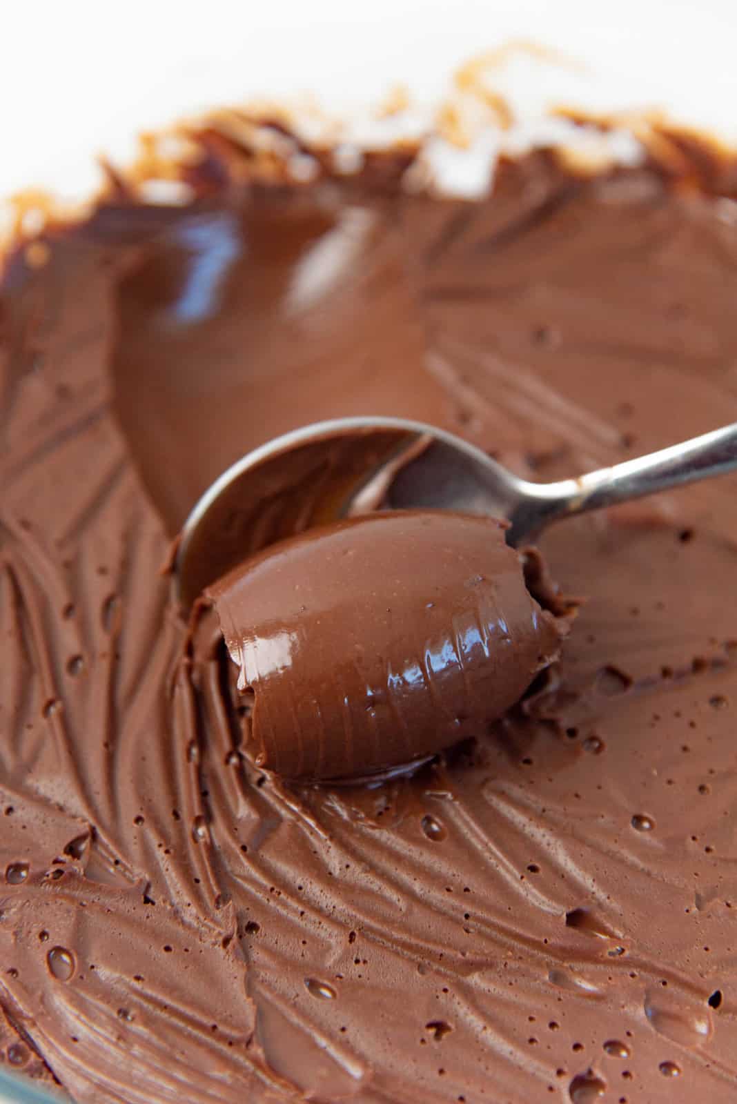 A close up of a spoon, scooping up the chocolate creameux, forming a shiny, smooth spiral of chocolate cremeux.