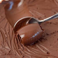 Chocolate cremeux being spooned from a container, creating a shiny curled ball of creameux on the spoon.