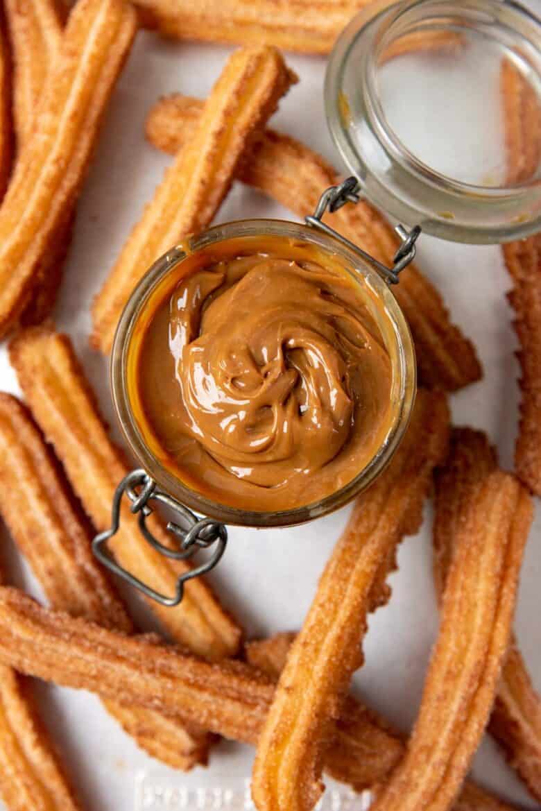 Overhead view of dulce de leche in a jar with churros in the background.