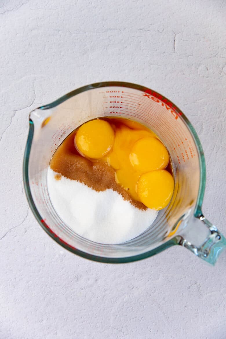 Overhead view of egg yolks, sugar and vanilla in a large jug prior to being mixed together.