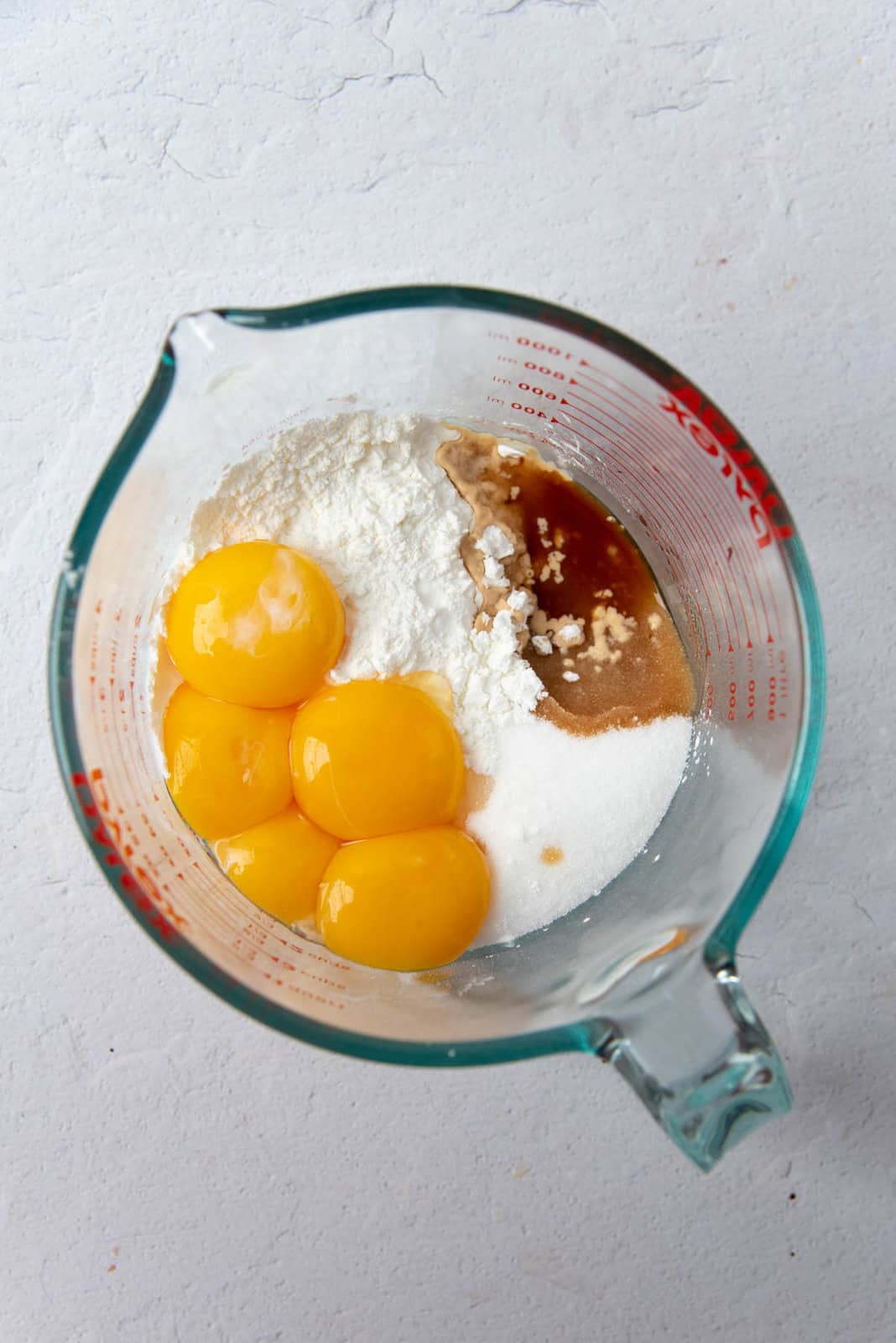 Egg yolks, cornstarch, vanilla and sugar placed in a large jug, overhead view.